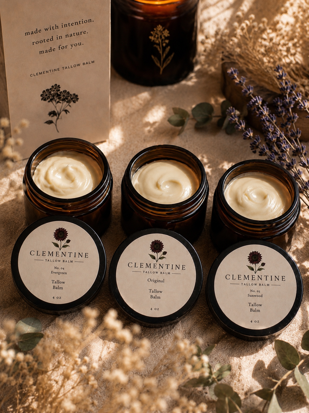 Three open jars of Clementine tallow balm arranged with lavender and dried botanicals in warm afternoon light